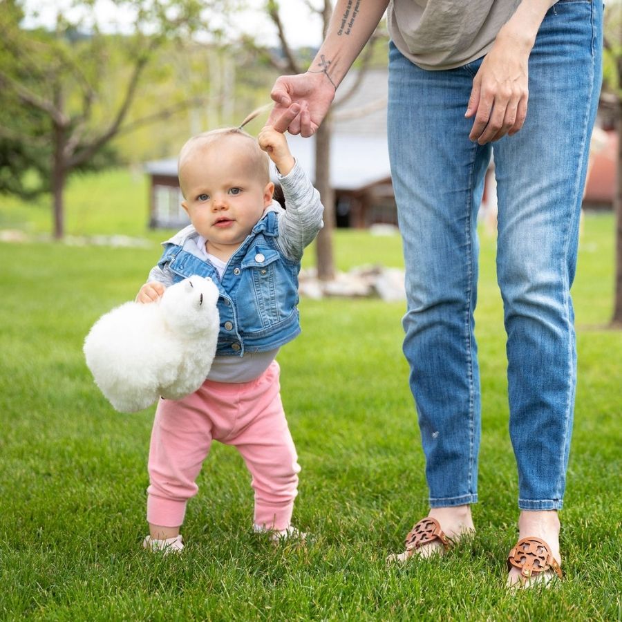 mom holding little girl's handing while she's holding a white alpaca wool plush toy
